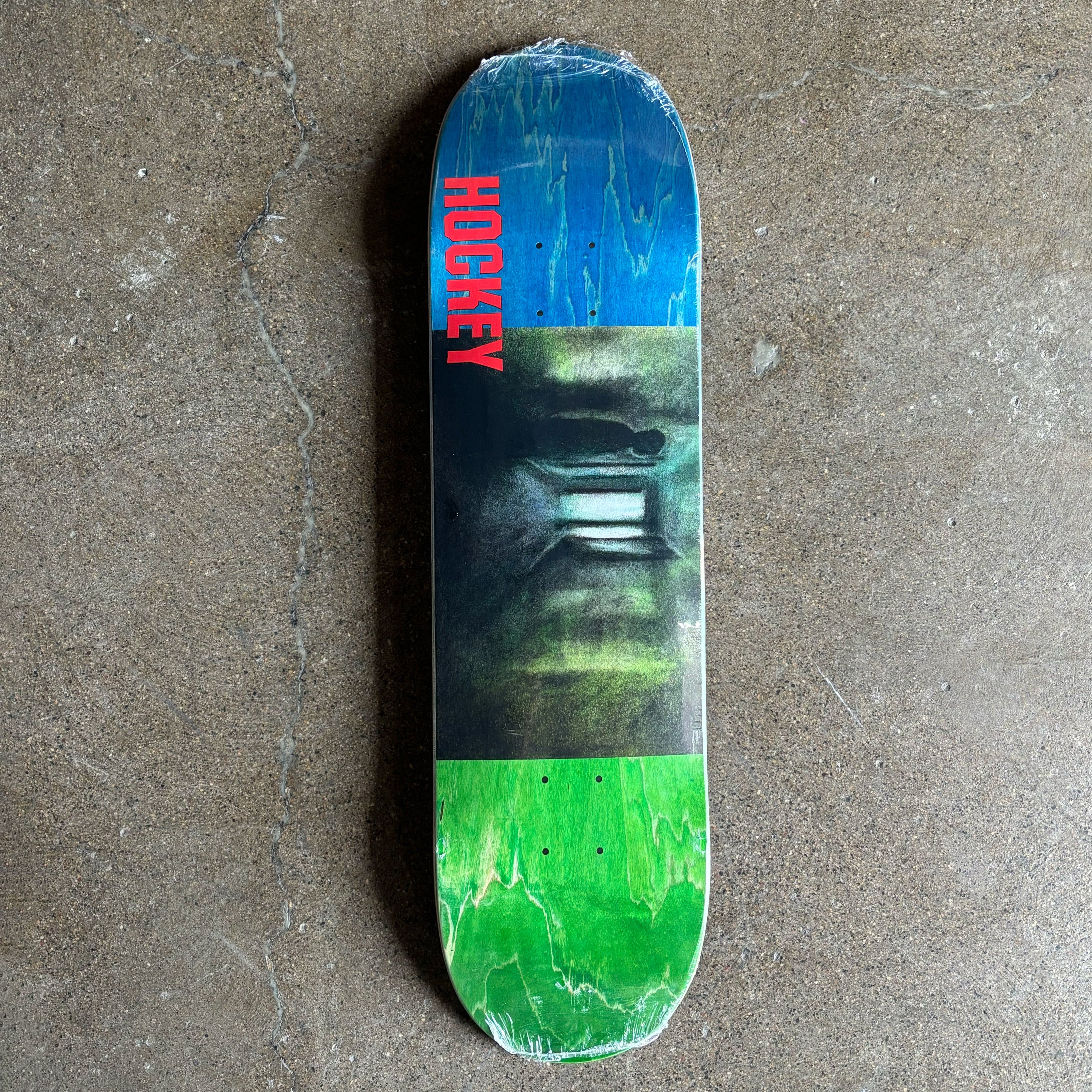 Skateboard deck with blue and green design on a concrete surface